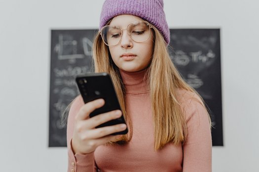 Jugendliches M&auml;dchen steht vor Tafel und schaut auf ihr Handy