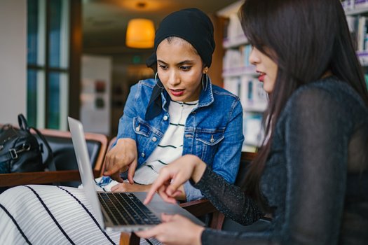 Junge Frau erkl&auml;rt anderer Frau etwas am ge&ouml;ffneten Notebook